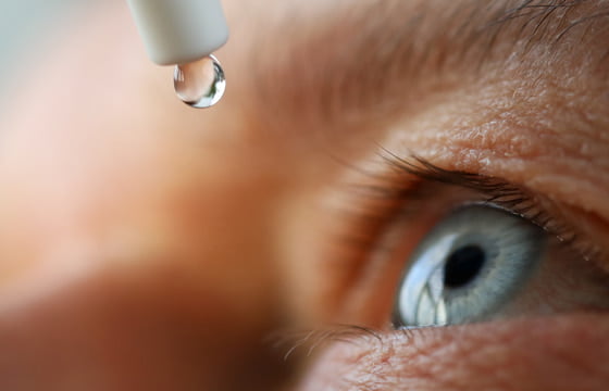 Older woman's eye closeup with liquid eyedrops being applied