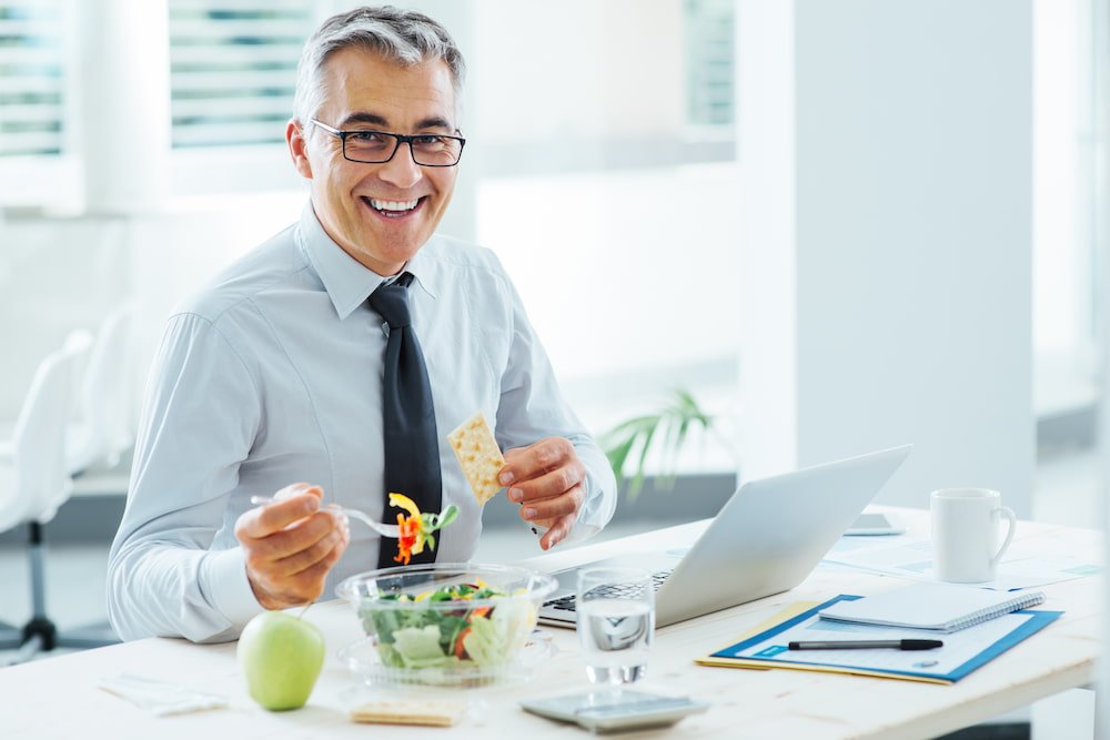 Middle age man eating salad while working from home